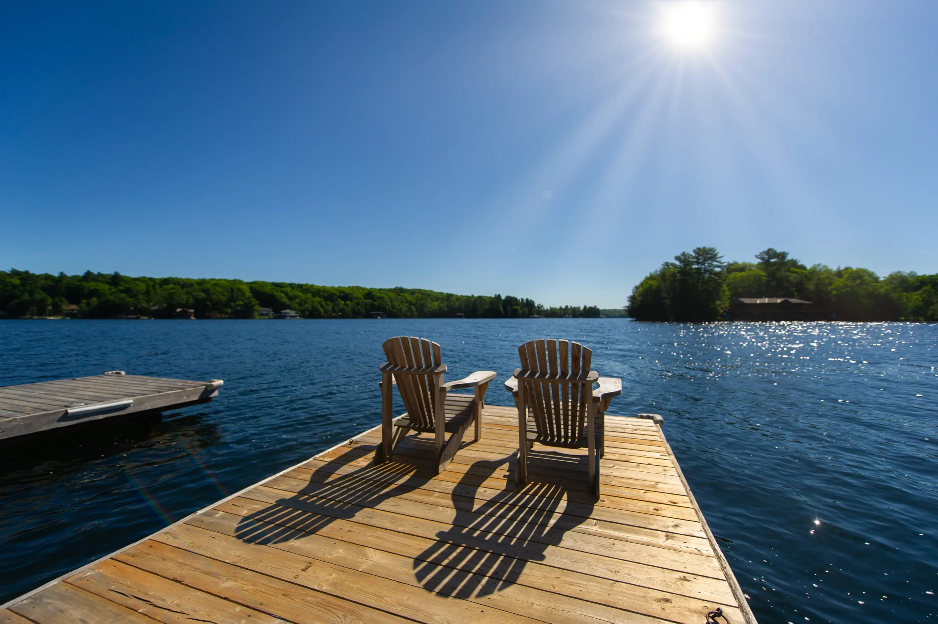 Sunrise on two empty Adirondack chairs Cottage life - Sunrise on two empty Adirondack chairs sitting on a dock on a lake in Muskoka, Ontario Canada. The sun light create long shadows on the wooden pier.